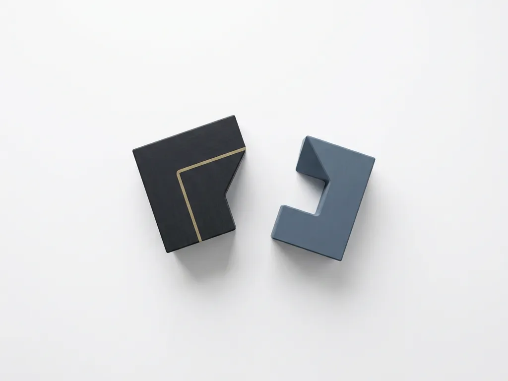 Twee niet-uitgelijnde geometrische puzzelstukken in houtskool en leisteenblauw zweven uit elkaar op een wit oppervlak.